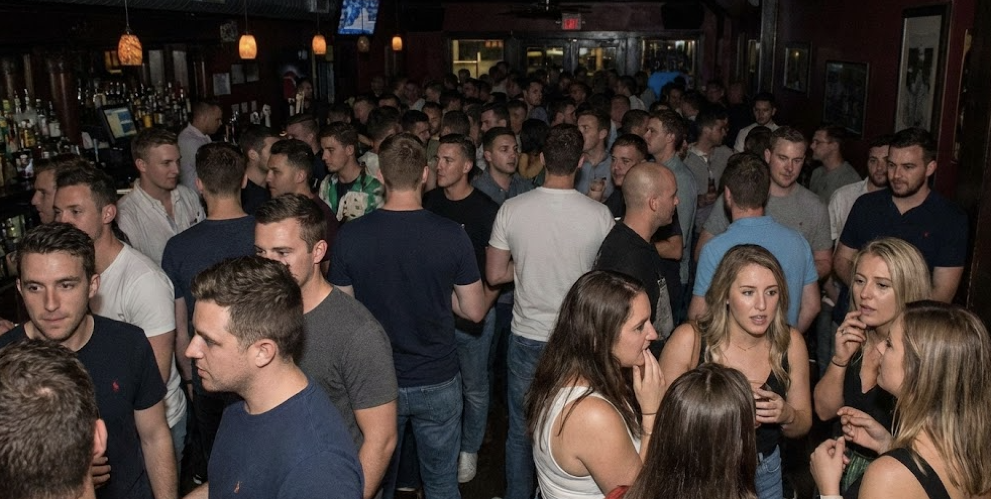 A crowded bar is full of people, mostly men, wearing casual clothes.
