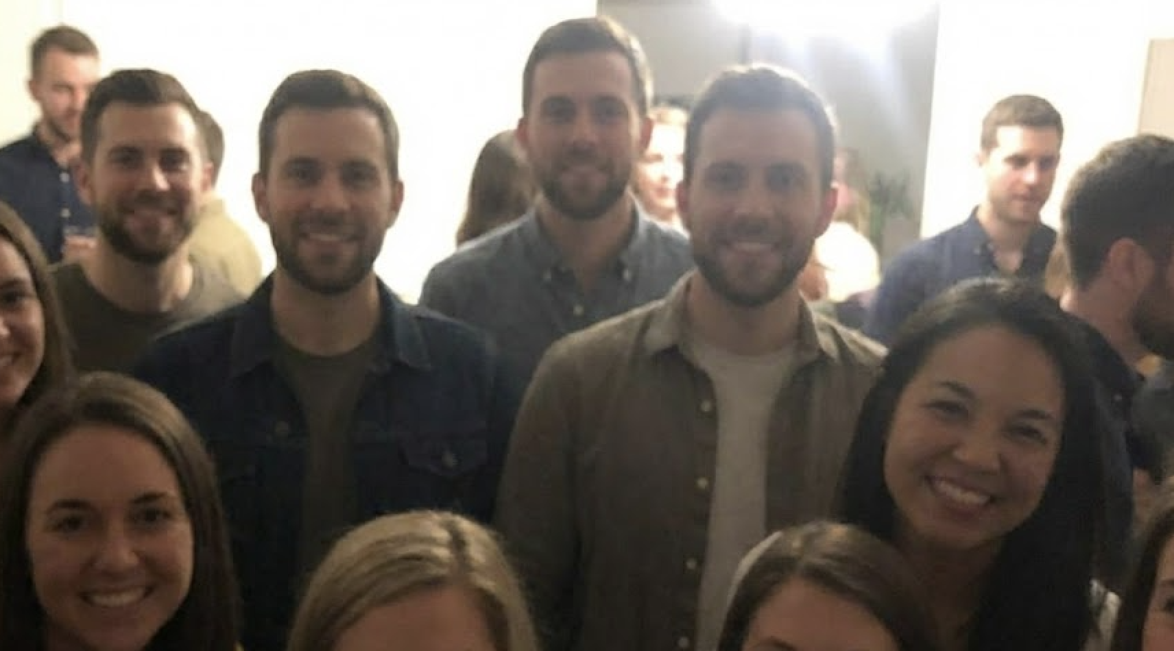 The image shows a group of people smiling indoors, with several men appearing multiple times.