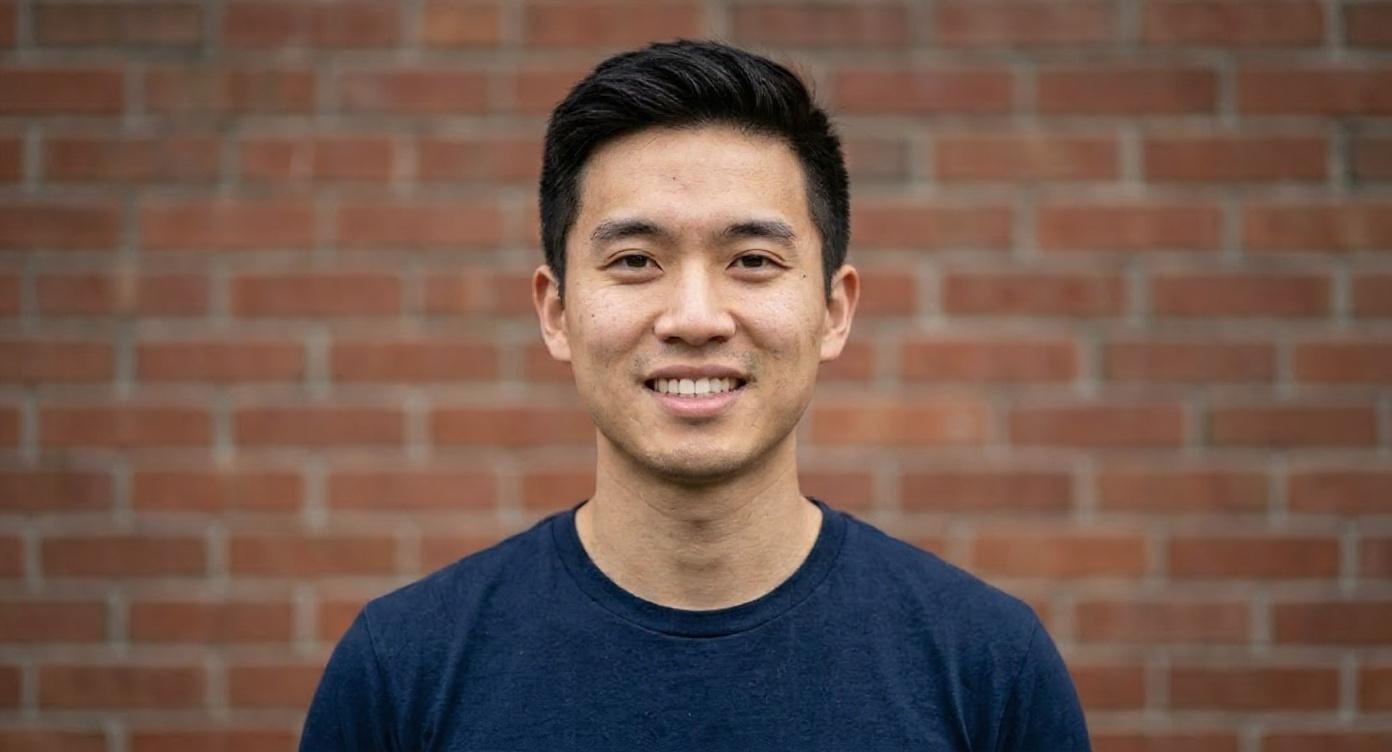 Portrait of smiling Asian man against a red brick wall.