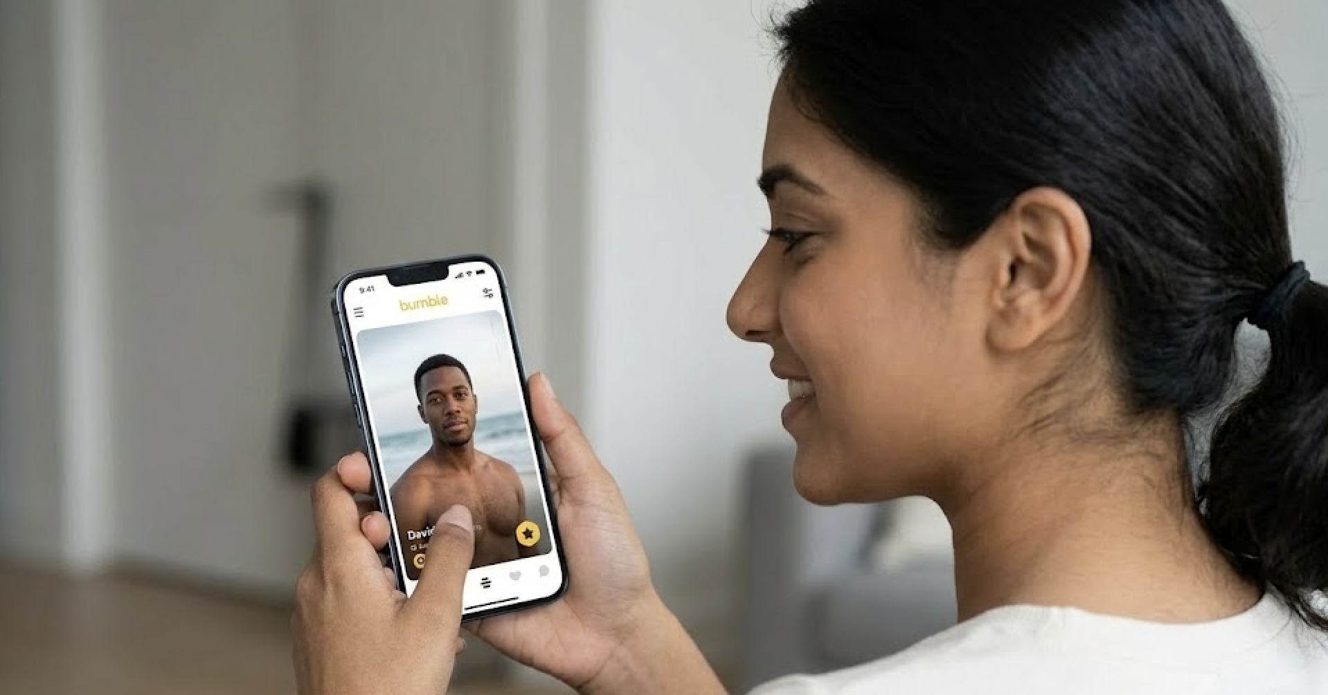 A smiling woman looks at a man's profile photo on the Bumble dating app.