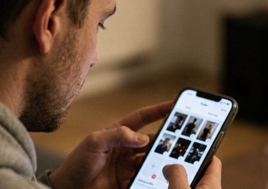 A man with stubble looks intently at a smartphone screen, using a fingers to tap.