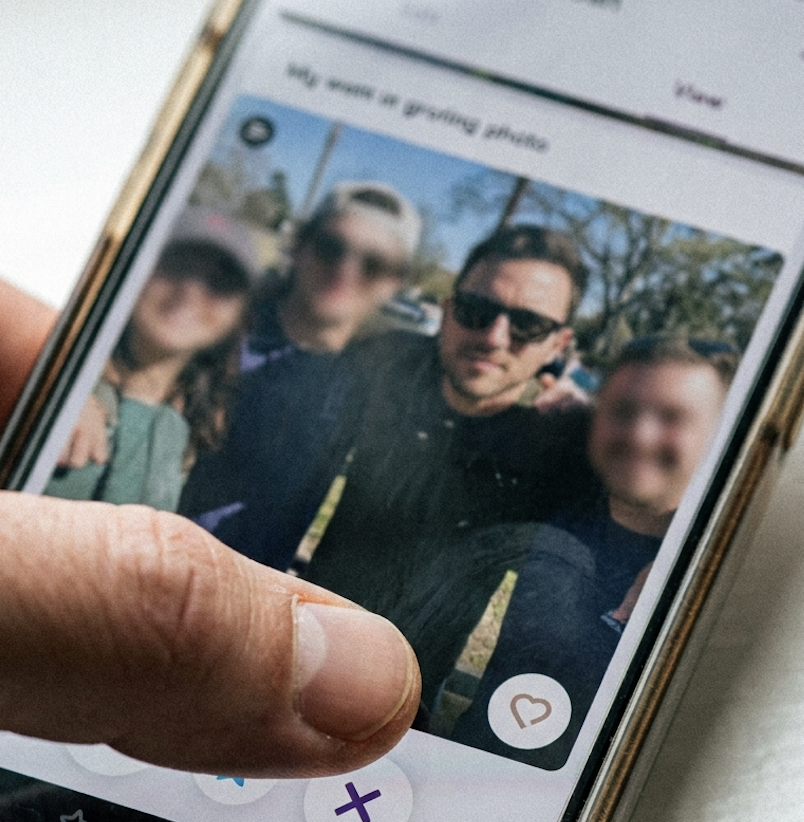 A hand holding a smartphone displays two men and two women in a group photo on a dating app.